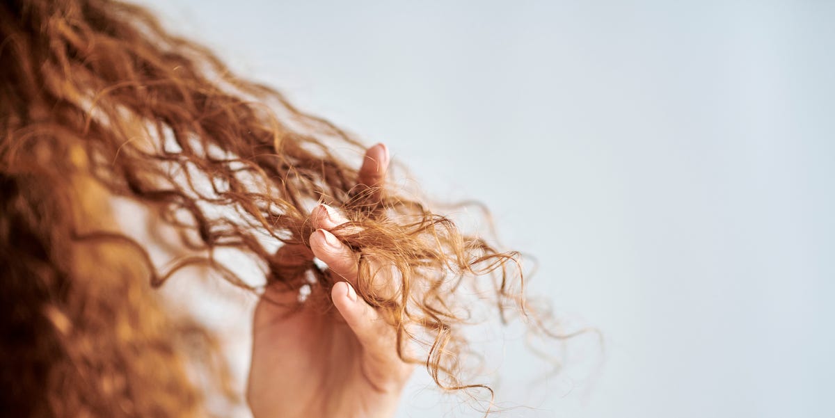 A woman gently holding her curly hair, showcasing natural texture, symbolizing hair care treatments like Brazilian protein.