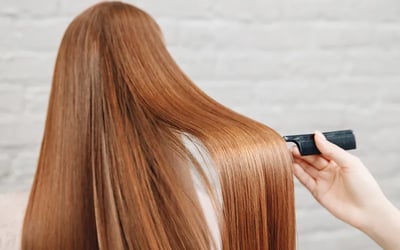 Hairdresser combing long, smooth, shiny auburn hair after a professional protein treatment.