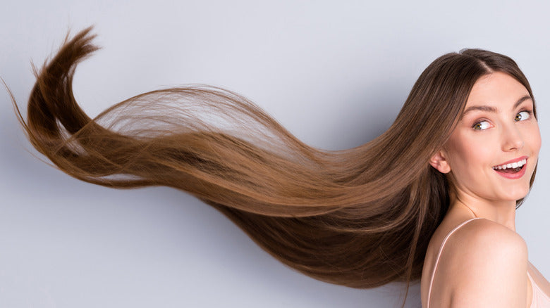 Smiling woman with long, smooth, shiny hair flipping it back, showing healthy results after hair botox treatment.